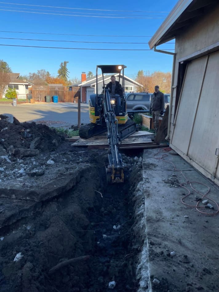 Mini-excavator digging a trench beside a Santa Rosa home for sewer line replacement