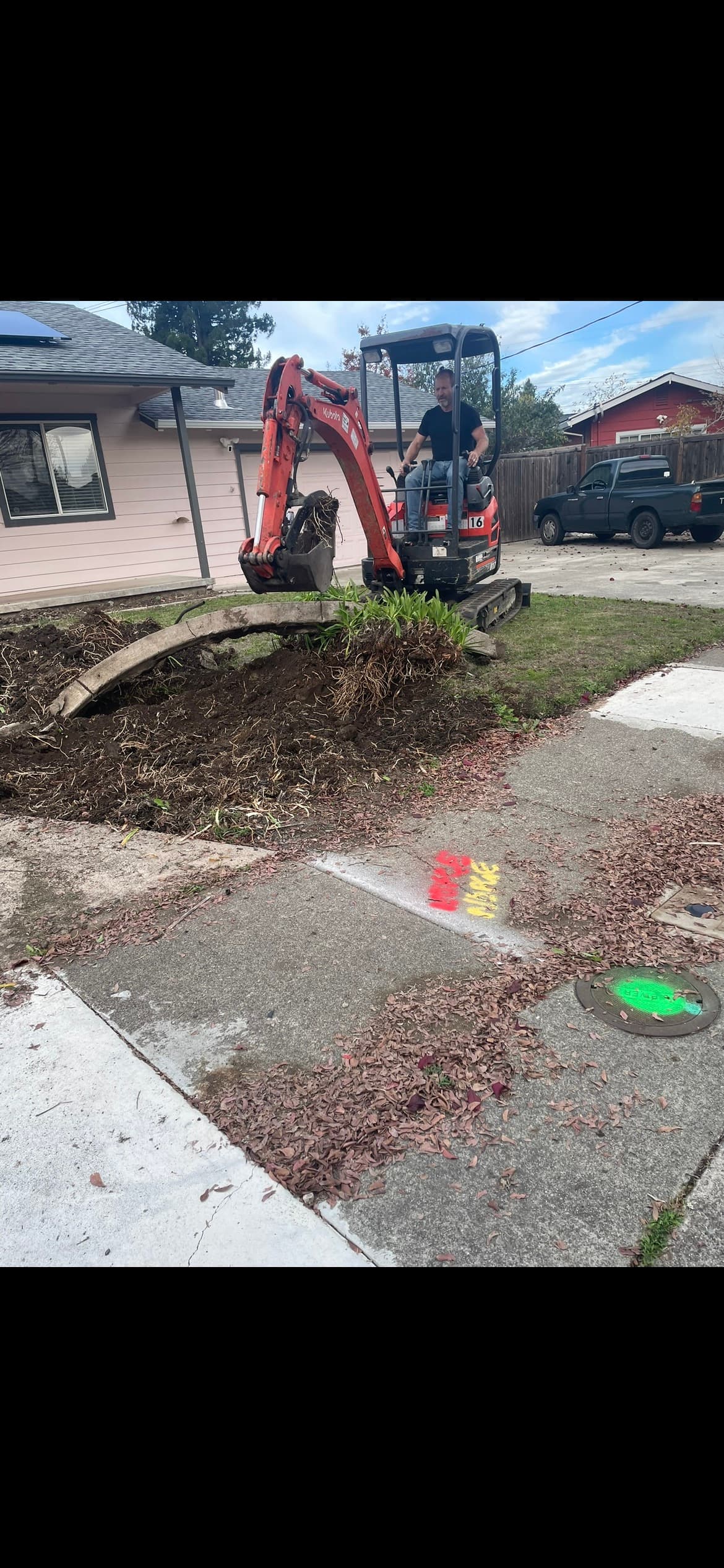 Mini-excavator digging up a drain line near a driveway in Santa Rosa