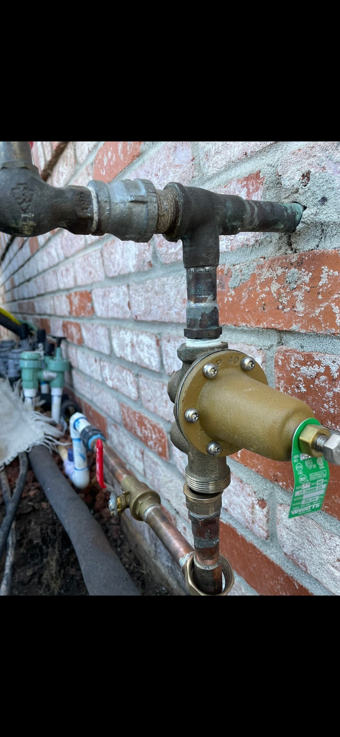 Close-up of a tankless water heater pressure regulator on an exterior brick wall